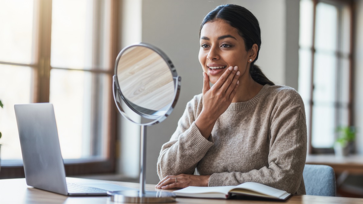 A student smiling at a table mirror while practising English sounds
